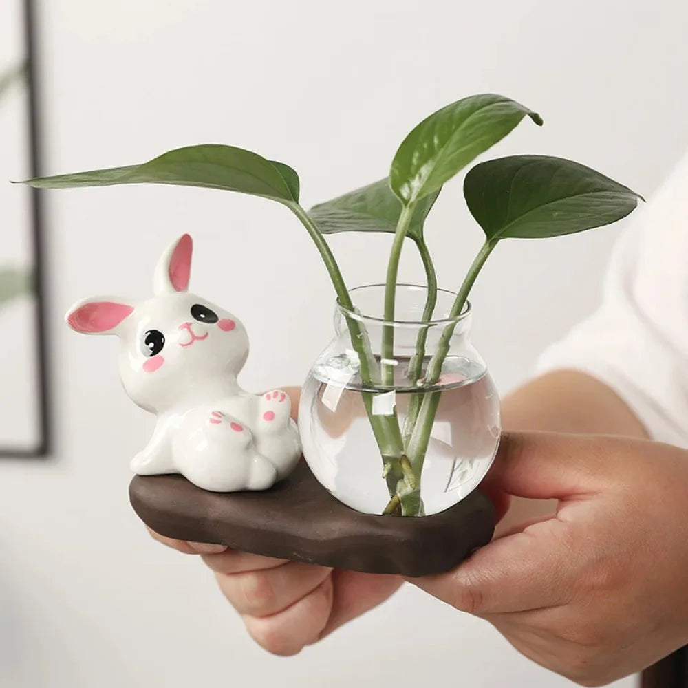 Bunny Glass Bud Vase: 01 sidelying bunny vase held in hands with green cuttings