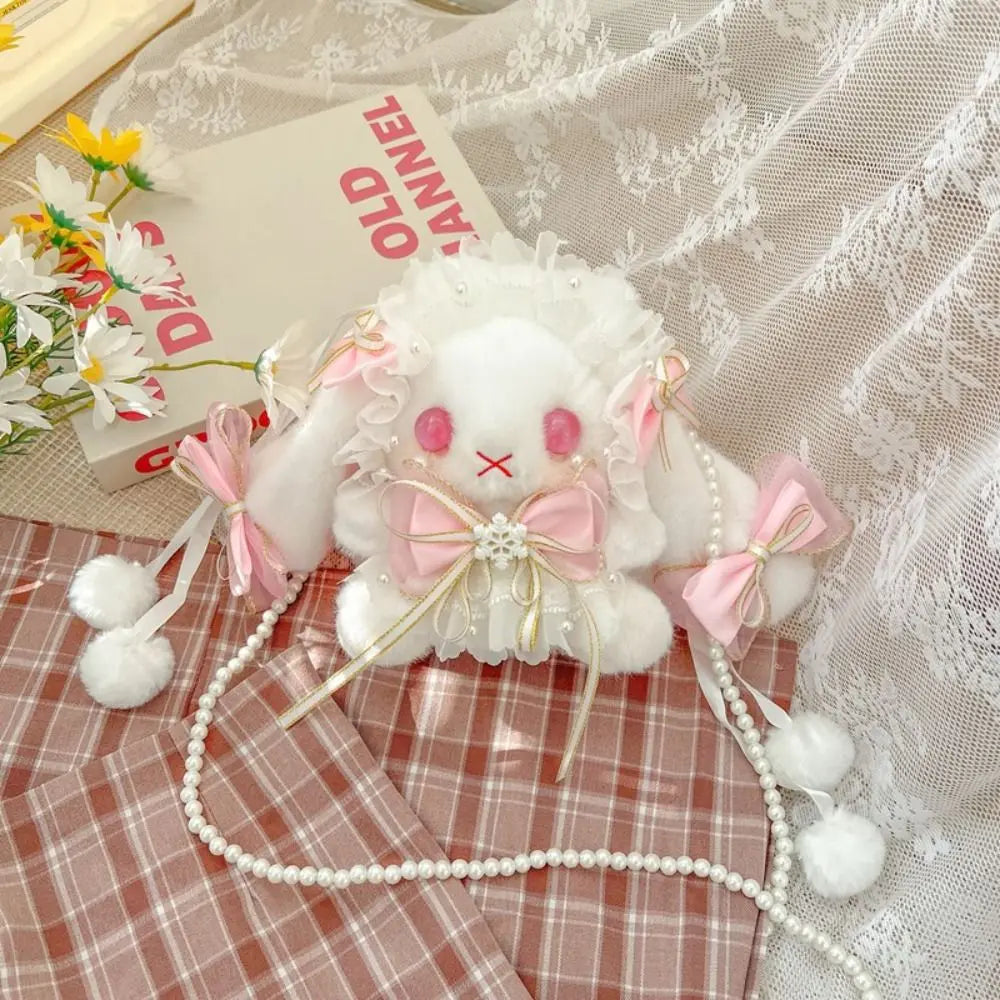 Lace Bow Bunny Plush Crossbody Bag: Pink bow bunny purse with dangling pom poms displayed on plaid fabric