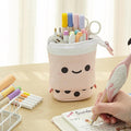 Pink smiling stand-up pencil case on a desk holding pens; pens not included