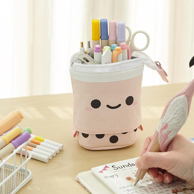 Pink smiling stand-up pencil case on a desk holding pens; pens not included