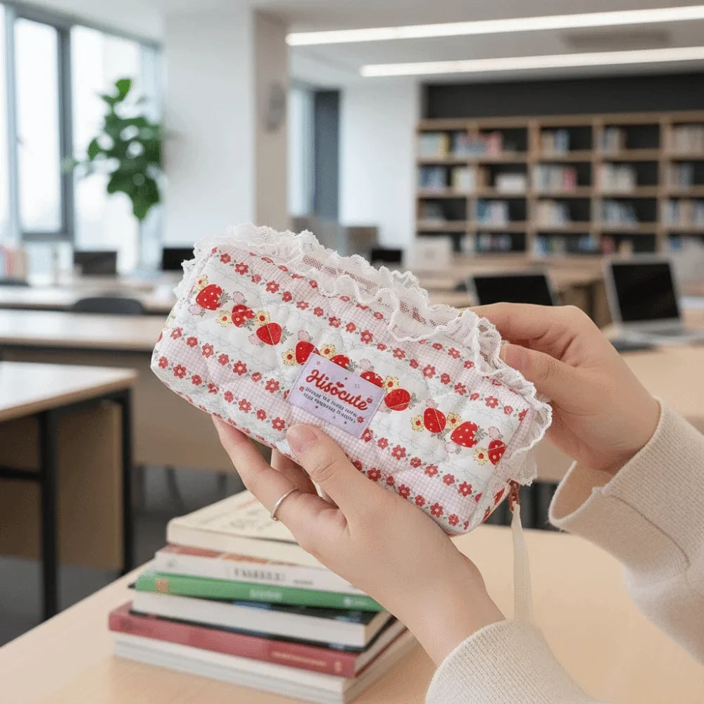 Quilted Ruffle Pencil Case: A strawberry print pencil case is held beside a stack of books in 13