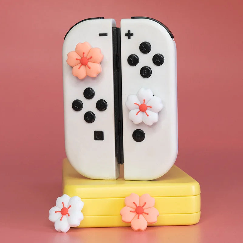 Sakura Flower Switch Thumb Grip Caps: White controllers wearing pink and white flower thumb grips on a yellow stand